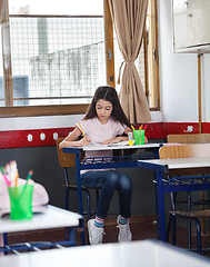 Image showing Schoolgirl Writing In Book At Desk In Classroom
