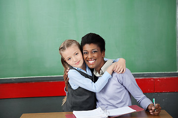 Image showing Happy Schoolgirl Hugging Teacher At Desk