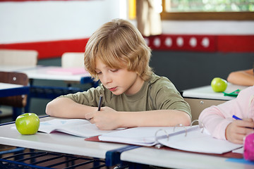 Image showing Schoolboy Writing On Book In Classroom