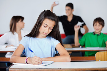 Image showing Schoolgirl Writing At Desk While Classmates Playing