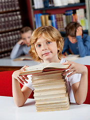 Image showing Schoolboy Sitting With Stack Of Books At Table In Library
