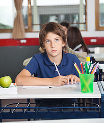 Image showing Schoolboy Looking Away While Writing At Desk