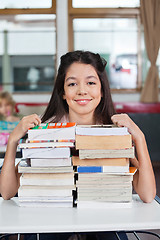 Image showing Schoolgirl Smiling With Stacked Books At Desk