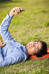 Image showing College Student Holding Mobilephone While Lying On Grass At Camp