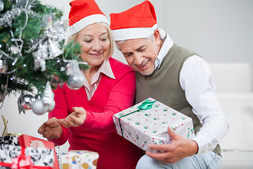 Image showing Senior Couple Looking At Present While Decorating Christmas Tree