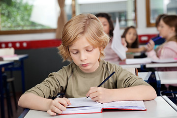 Image showing Schoolboy Writing In Book At Desk