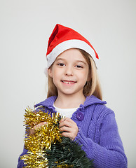 Image showing Smiling Girl Wearing Santa Hat Holding Tinsels