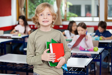 Image showing Schoolboy Holding Books With Classmates In Background