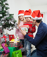 Image showing Parents Giving Gift To Boy By Christmas Tree