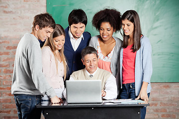 Image showing Professor And Students Looking At Laptop In Classroom