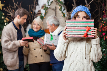 Image showing Thoughtful Woman Holding Christmas Present With Family In Backgr