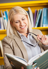 Image showing Female Librarian Holding Glasses While Reading Book In Library