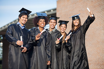 Image showing Students In Graduation Gowns Holding Diplomas On University Camp