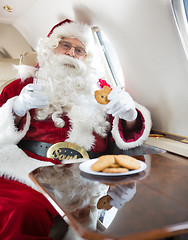 Image showing Santa Eating Cookies While Holding Milk Glass In Private Jet