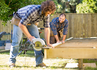 Image showing Carpenter Looking At Coworker While Assisting Him In Cutting Woo