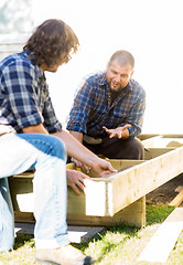 Image showing Carpenter Communicating With Coworker Measuring Wooden Frame