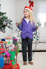 Image showing Girl Holding Fairy Lights While Standing By Christmas Gifts