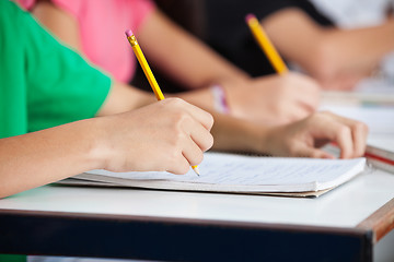 Image showing Classmates Writing In Book At Desk