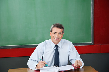 Image showing Happy Teacher With Binder And Pen Sitting At Desk