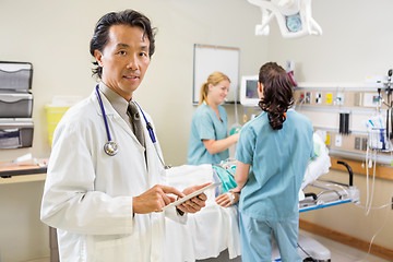 Image showing Doctor Holding Digital Tablet While Nurses Examining Patient