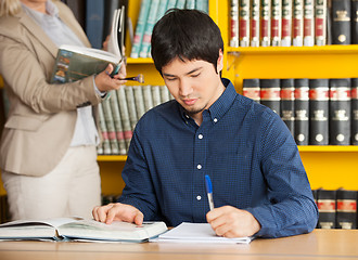 Image showing Student Writing In Book At College Library