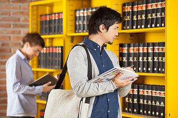 Image showing Student Holding Books While Looking At Shelf In Library
