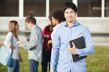 Image showing Man Holding Book With Students In Background On Campus
