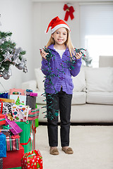 Image showing Girl Holding Fairy Lights While Standing By Christmas Presents
