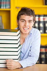 Image showing Confident Man With Piled Books Smiling In College Library