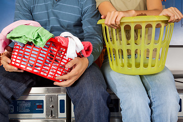 Image showing Couple With Laundry Baskets Sitting On Washing Machines