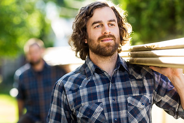 Image showing Carpenter Carrying Planks While Looking Away