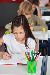 Image showing Schoolgirl Writing In Book At Classroom