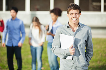 Image showing Man Holding Books With Students In Background On Campus