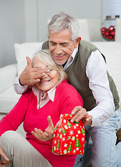 Image showing Senior Man Covering Woman's Eyes While Giving Christmas Gift