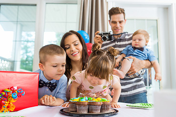 Image showing Family Watching Girl Blowing Out Candles On Birthday Cake