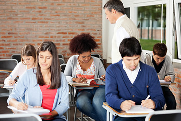 Image showing Students Writing Exam While Teacher Supervising Them In Classroo