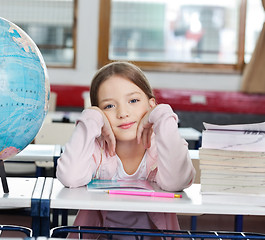 Image showing Schoolgirl With Stack Of Books And Globe At Desk