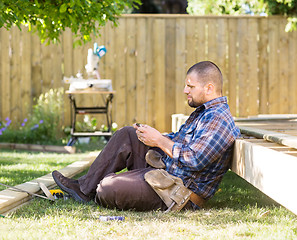 Image showing Carpenter Messaging On Cellphone While Leaning On Wooden Frame