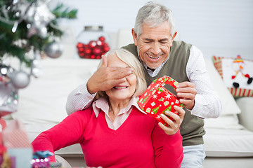 Image showing Senior Man Covering Woman's Eyes While Giving Christmas Present