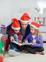 Image showing Father And Children In Santa Hats Reading Book