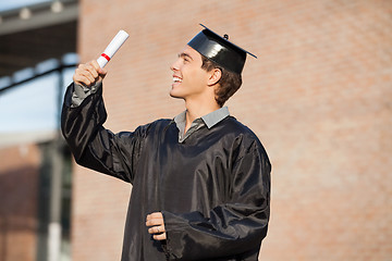 Image showing Man In Graduation Gown Looking At Certificate On Campus