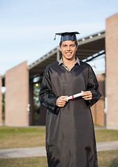 Image showing Man In Graduation Gown Holding Diploma On College Campus