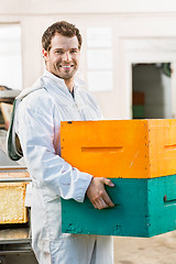 Image showing Happy Male Beekeeper Carrying Stack Of Honeycomb Crates