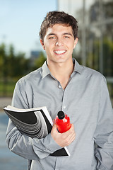 Image showing Male Student With Juice Bottle And Book Standing On Campus