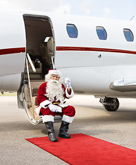 Image showing Santa Toasting Milk Glass While Sitting On Private Jet's Ladder