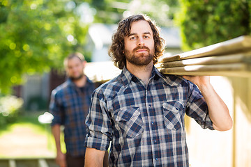 Image showing Carpenter With Coworker Carrying Wooden Planks Outdoors