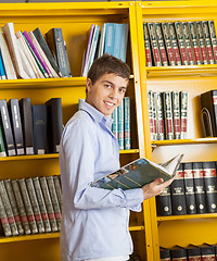 Image showing Male Student With Book Standing Against Shelf In Library