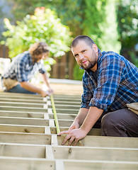 Image showing Carpenter Measuring Wood With Tape While Coworker Helping Him