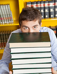 Image showing Male Student Peeking Over Stacked Books In Library