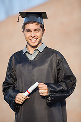 Image showing Happy Man In Graduation Gown Holding Certificate On Campus